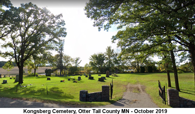 The Kongsberg Cemetery, Otter Tail County MN: Color photo, taken in October 2019, of a small, green-lawned cemetery containing several gravestones behind an open double iron gate hinged to two large stone posts; the land slopes down behind trees to farm fields in the distance